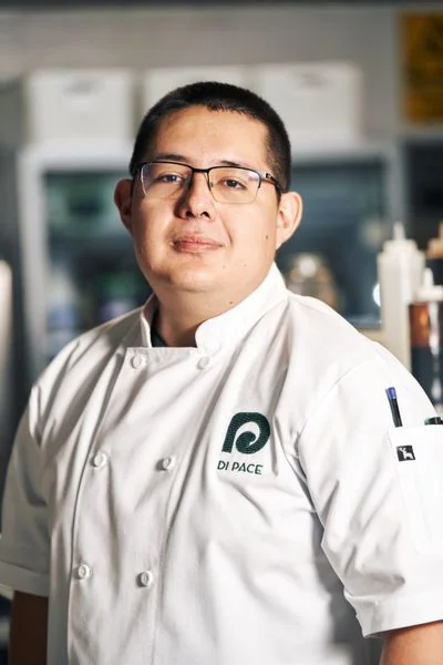Chef de Cuisine in pristine white uniform overseeing kitchen preparations